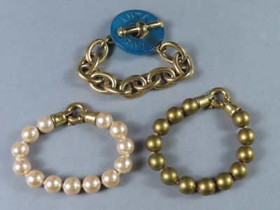 trois bracelets ornés de perles et d'un bouton bleu sur un fond gris