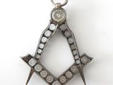 a close up of a masonic square and compass pendant on a white surface
