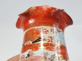 a hand holding a vase with a red and white design
