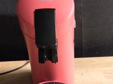 a pink coffee maker sitting on a table next to a black wall