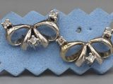 deux paires de boucles d'oreilles en forme de nœud, en argent et diamants, posées sur un morceau de tissu bleu