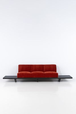 a red couch sitting on top of a black table next to a white wall