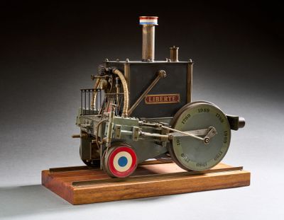 une petite maquette de machine à vapeur posée sur un socle en bois