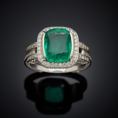 an emerald and diamond ring on a black surface