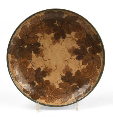 une assiette marron et verte décorée de feuilles, posée sur une surface blanche