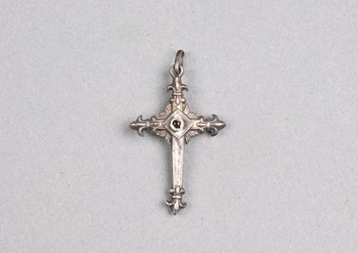 une croix argentée avec une pierre noire au centre, sur fond blanc