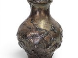 a silver vase that is sitting on a white surface
