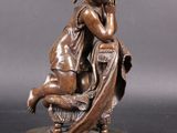 an antique bronze statue of a woman sitting on a chair
