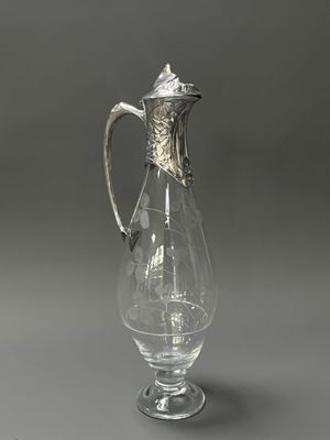 un pichet ancien en verre muni d'une anse en argent, sur fond gris