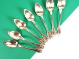 six cuillères en argent sont disposées en cercle sur un fond vert et blanc