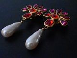 two pairs of earrings with red and white stones on a black surface