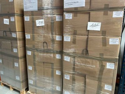 Plusieurs piles de cartons sont empilées sur des palettes dans un entrepôt