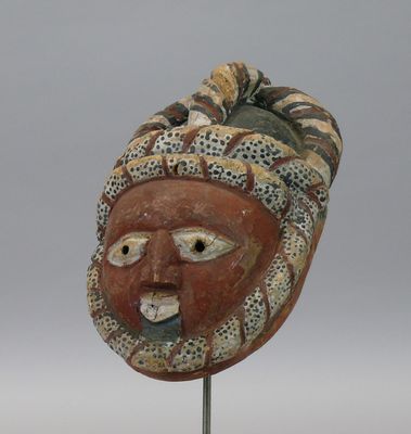 un masque en bois posé sur un socle en métal, sur fond gris
