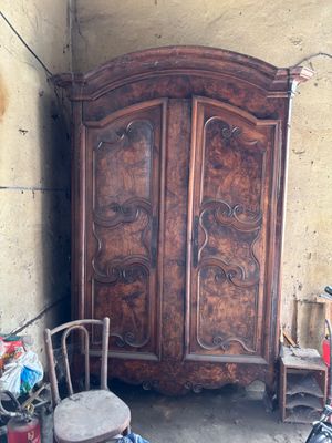 a wooden armoire in the corner of a room with a chair and a stool