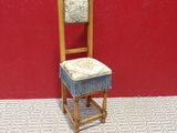 une petite chaise en bois avec un coussin dessus, devant un mur rouge