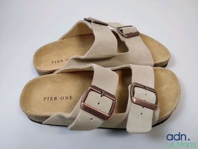 une paire de sandales beiges ornées de deux boucles, posées sur une surface blanche