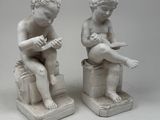 pair of white statues of a boy and a girl sitting on stools