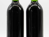 two bottles of red wine sitting next to each other on a white surface