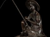 bronze statue of a boy sitting on a rock with a fishing pole