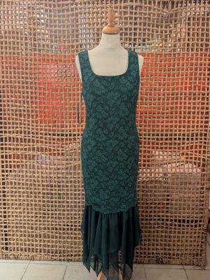 a green dress on a mannequin stand in front of a woven wall