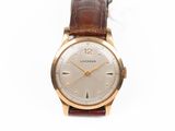 gros plan d'une montre sur une surface blanche avec un bracelet marron