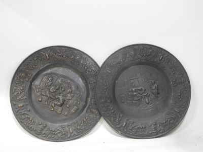 deux assiettes noires ornées de motifs, posées sur une surface blanche