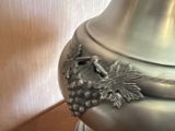 a silver vase sitting on a wooden table next to a cell phone