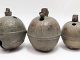 trois vieilles cloches en métal posées les unes à côté des autres sur une surface blanche