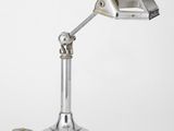 une lampe de bureau argentée sur un fond blanc, avec son cordon branché