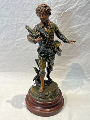 statue en bronze représentant un garçon avec un oiseau, posée sur un socle en bois