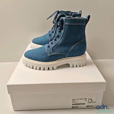 Des bottes en jean bleu à semelles blanches sont posées sur une boîte blanche