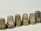 six antique thimbles lined up in a row on a white surface