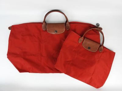 deux sacs rouges munis de poignées marron, posés sur une surface blanche