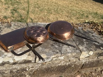 des casseroles et des poêles sont posées sur un rebord en pierre à l'extérieur