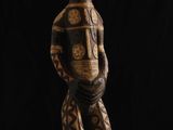 une statue en bois représentant un homme debout devant un fond noir