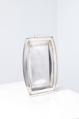 assiette rectangulaire en argent posée sur un socle blanc, avec un fond blanc