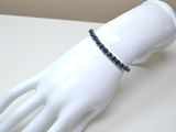 une main de mannequin blanche ornée d'un bracelet en perles noires
