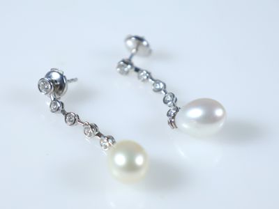 une paire de boucles d'oreilles en perles et diamants posées sur un fond blanc