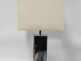 une lampe de table chromée surmontée d'un abat-jour blanc