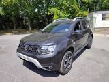 a grey dacia parked in a parking lot with trees in the background