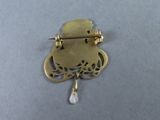 a close up of a gold brooch with a pearl hanging from it