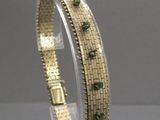 un gros plan sur un bracelet en or orné de pierres vertes