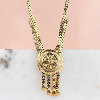 a gold necklace with a medallion and tassels on a marble surface