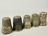 six antique thimbles lined up in a row on a white surface