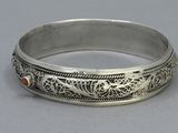 a close up of a silver bracelet with a red stone in the center