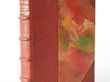 an old book with a red cover sitting on top of a white surface