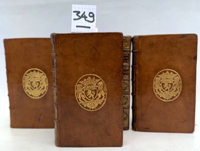 trois livres en cuir marron ornés de médaillons dorés, posés sur une surface blanche