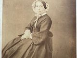 an old photo of a woman in a dress sitting on a chair