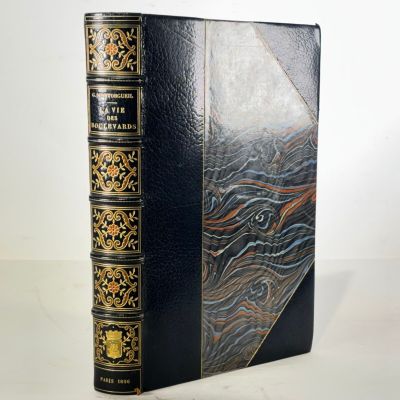an old book with a black cover and gold trim on a white surface