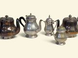cinq théières en argent et une cafetière posées sur une table